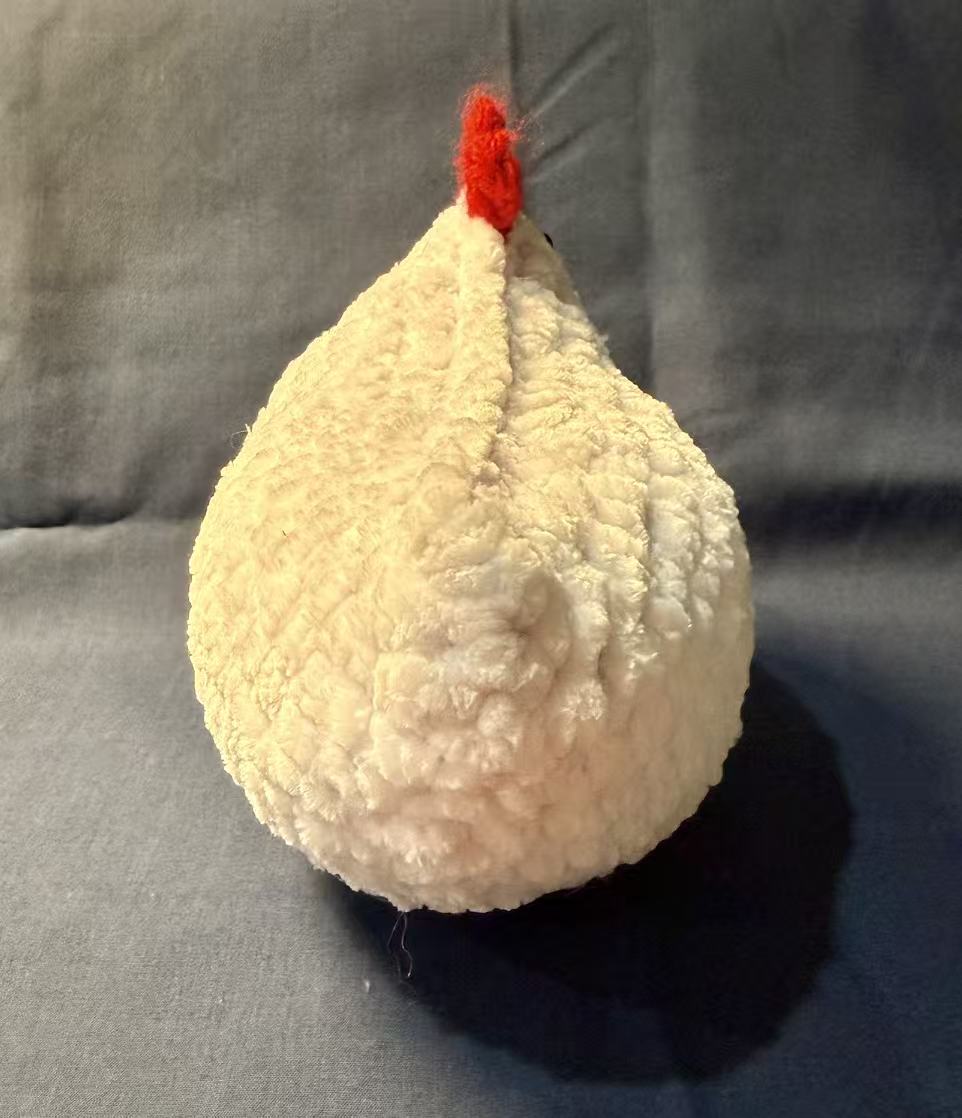 Back view of the white crochet chicken, showing its rounded body and bright red comb.